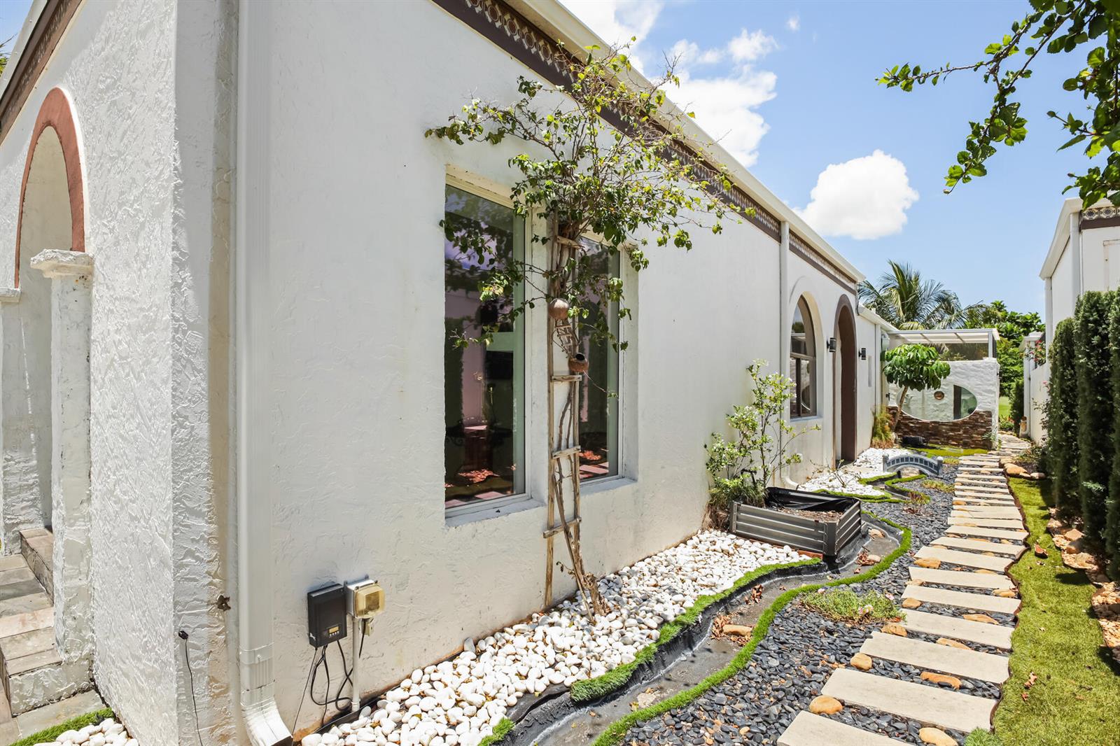 A white stucco house exterior features a stone path, a decorative dry creek, and landscaping — LAKE WORTH, FL