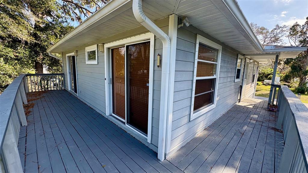 A gray house exterior features a wrap-around wooden deck and sliding glass doors — 7815 BUTLER AVENUE, HUDSON, FL