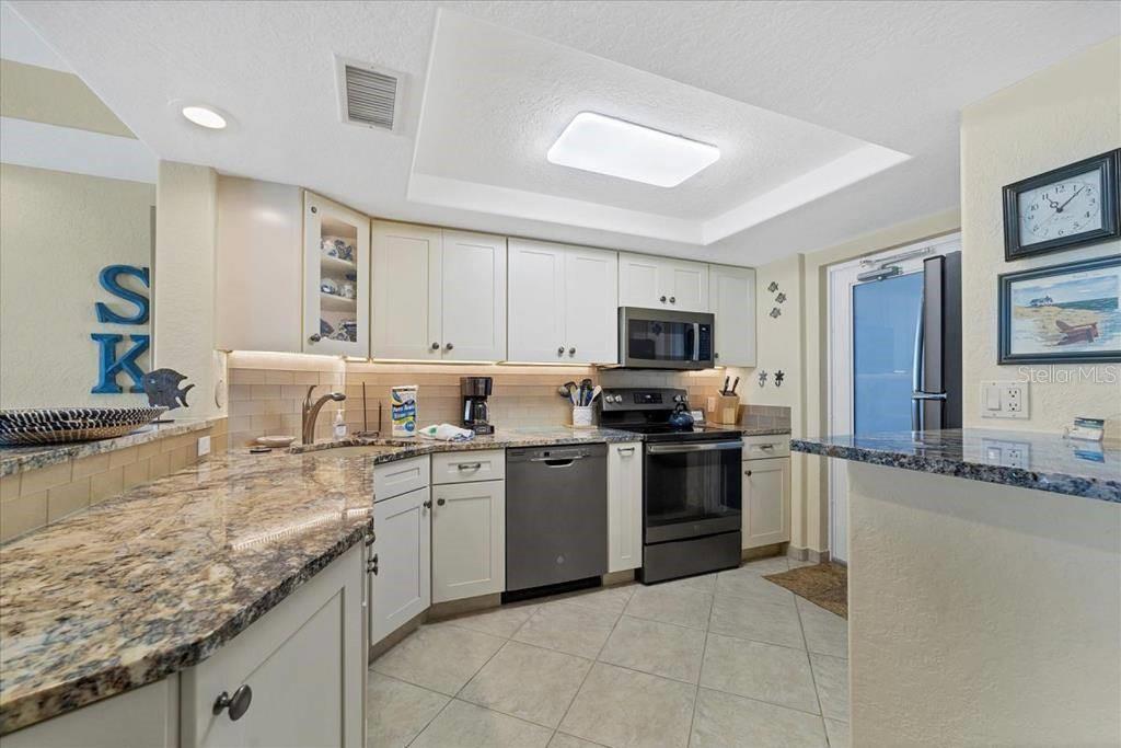 A kitchen features white cabinets, granite countertops, stainless steel appliances, and tile flooring — 6154 MIDNIGHT PASS ROAD UNIT 102, SARASOTA, FL