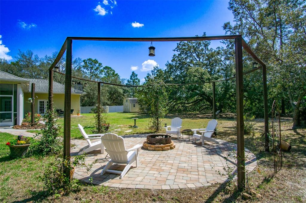 A backyard features a circular paver patio with a fire pit and four Adirondack chairs — 11092 MIRAGE AVENUE, WEEKI WACHEE, FL