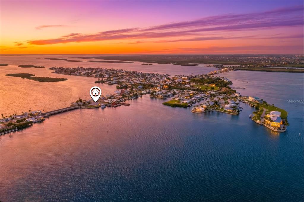 An aerial view of a coastal neighborhood at sunset with a house location marker — 4767 PINE ISLAND ROAD NW, MATLACHA, FL