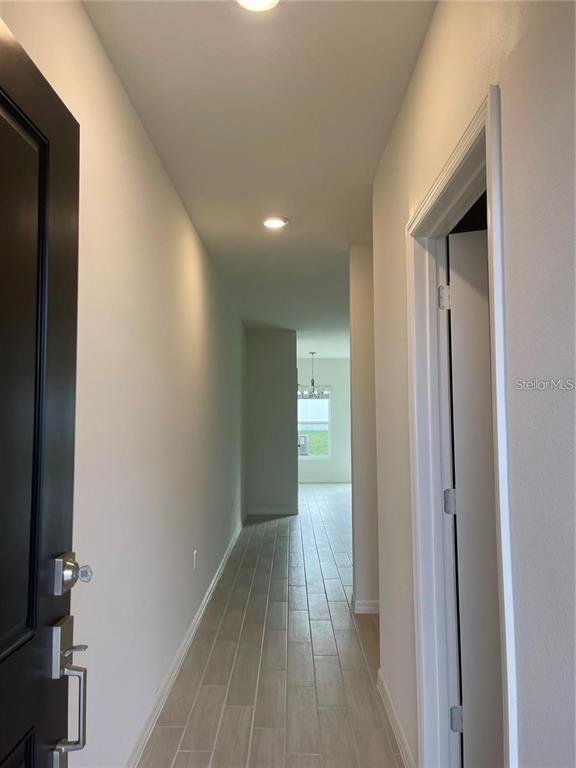 A hallway with light-colored tile flooring leads from an entryway toward a distant window — 1452 MIRABELLA CIRCLE, DAVENPORT, FL