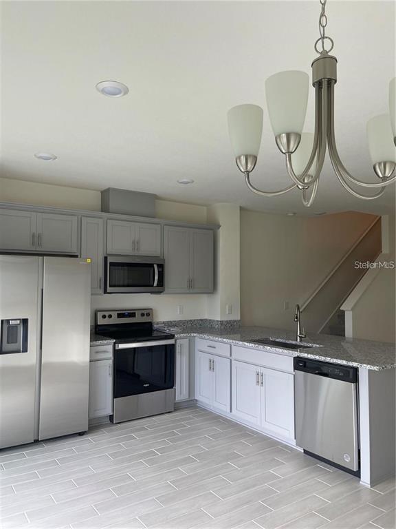 A kitchen features gray cabinets, stainless steel appliances, granite countertops, and a dining area chandelier — 1452 MIRABELLA CIRCLE, DAVENPORT, FL