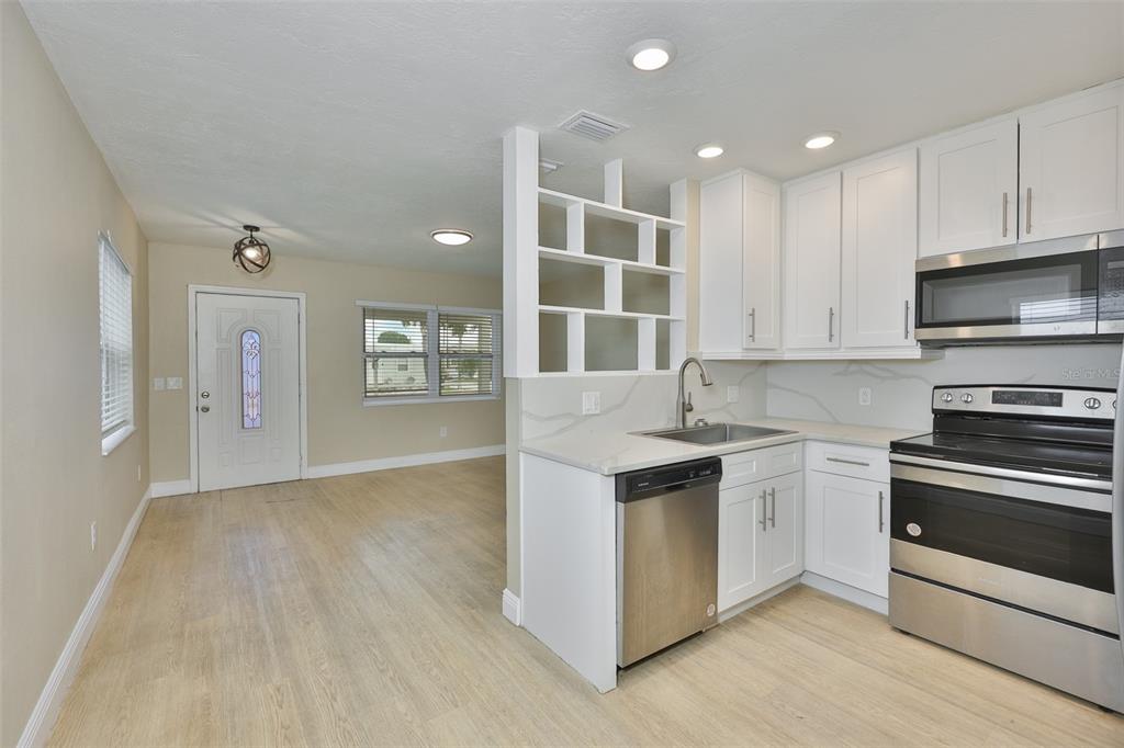 A kitchen with white cabinets and stainless steel appliances opens into a living area — 2450 40TH AVENUE N, ST PETERSBURG, FL