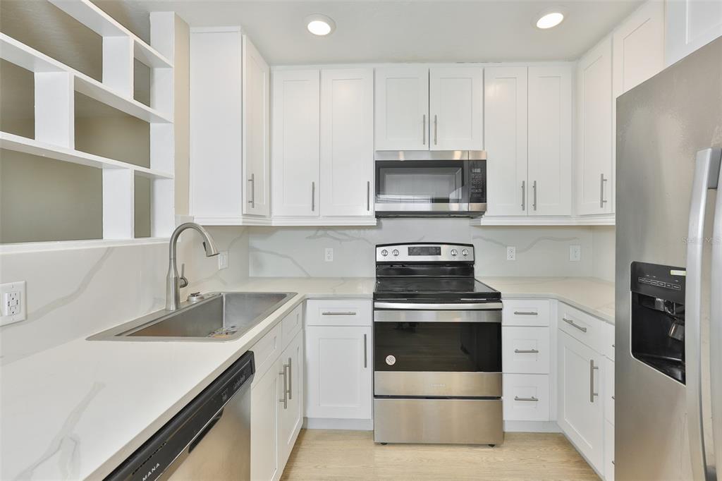 A kitchen features white cabinets, stainless steel appliances, and light-colored countertops with a backsplash — 2450 40TH AVENUE N, ST PETERSBURG, FL