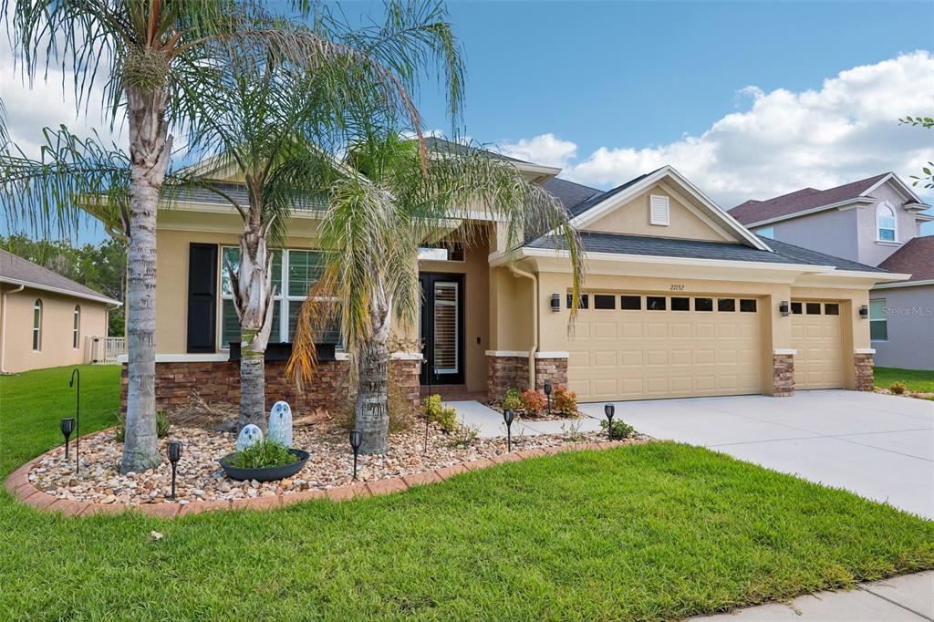 A single-story house with a tan stucco exterior, stone accents, and a three-car garage — 27152 SORA BOULEVARD, WESLEY CHAPEL, FL