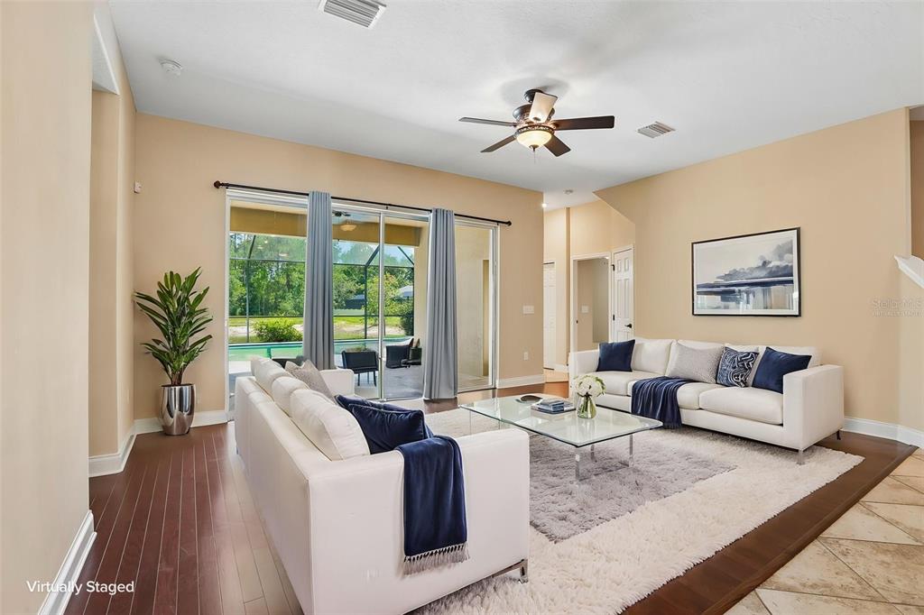 A living room with white sofas, a glass coffee table, and sliding doors to a pool — 27152 SORA BOULEVARD, WESLEY CHAPEL, FL