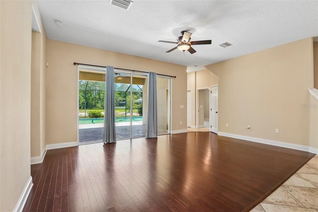 A living room with dark hardwood floors, a ceiling fan, and sliding glass doors — 27152 SORA BOULEVARD, WESLEY CHAPEL, FL