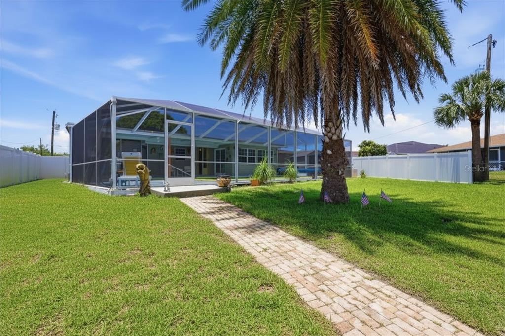 A backyard features a brick walkway leading to a screened-in patio and a palm tree — 201 E TARPON BLVD NW, PORT CHARLOTTE, FL