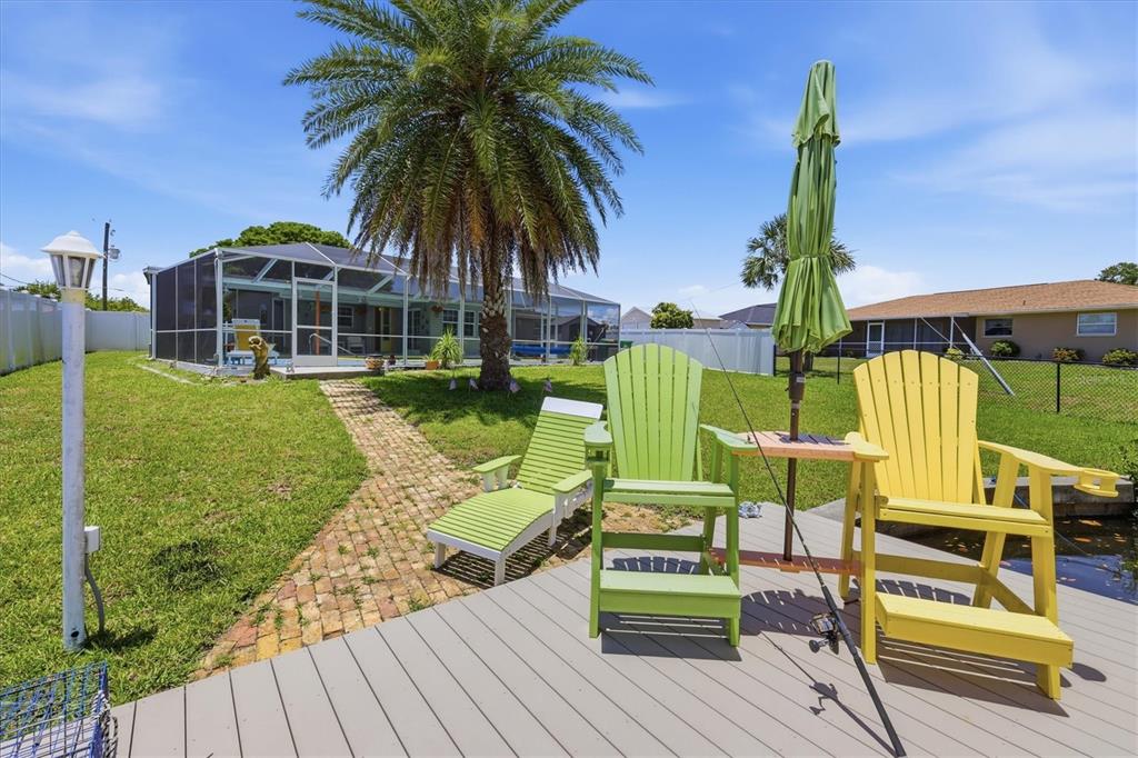 A backyard features a wooden deck with chairs, a brick path, and a screened-in patio — 201 E TARPON BLVD NW, PORT CHARLOTTE, FL