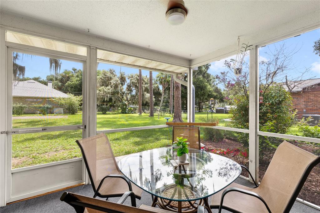 A screened-in porch with a glass-top table, chairs, and a view of a grassy backyard — 109 CARDINAL LANE, EUSTIS, FL