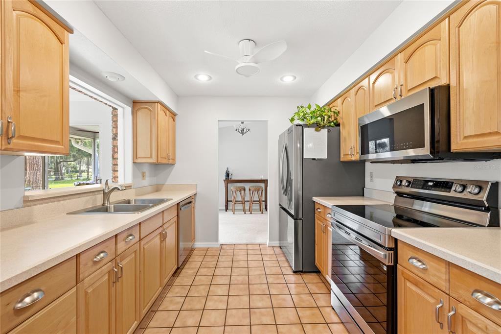 A kitchen with light wood cabinets, stainless steel appliances, and tan tile flooring — 109 CARDINAL LANE, EUSTIS, FL