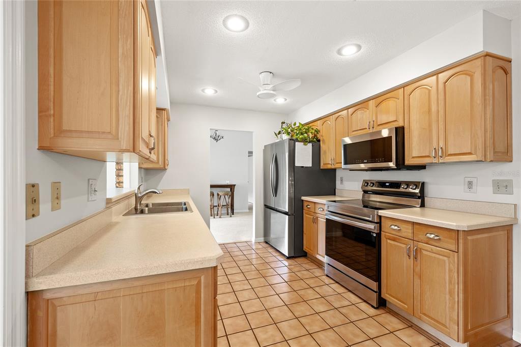 A kitchen with light wood cabinets, stainless steel appliances, and tan tile flooring — 109 CARDINAL LANE, EUSTIS, FL