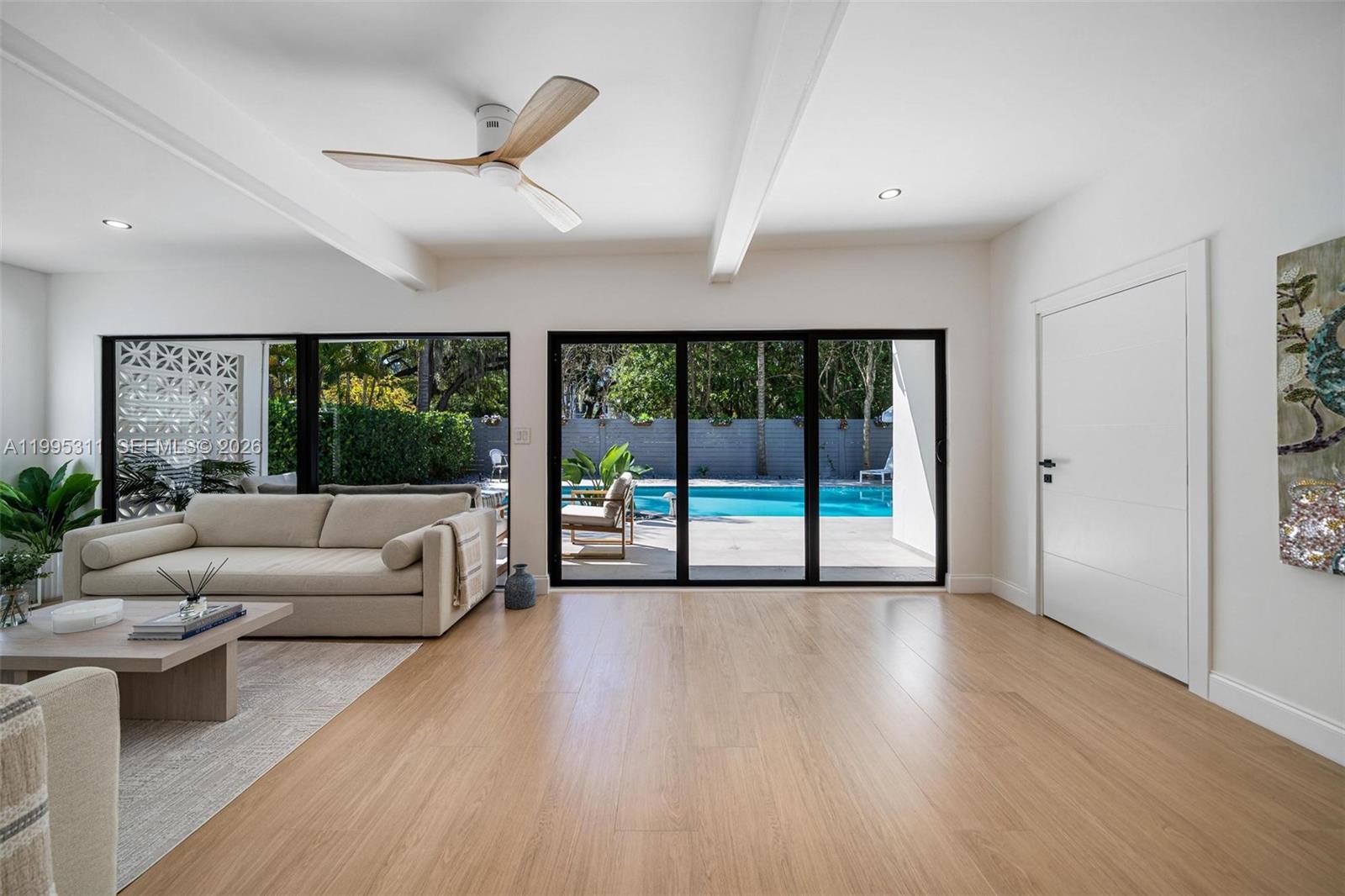A bright living room features light wood flooring, a ceiling fan, and sliding glass doors — 696 NE 67th St, Miami FL 33138, MIAMI, FL