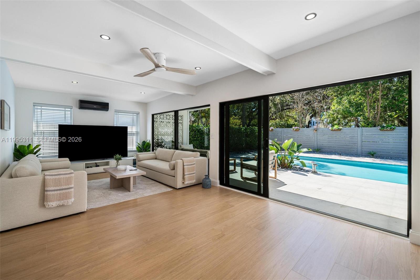 A living room with light wood floors features a pool view through sliding glass doors — 696 NE 67th St, Miami FL 33138, MIAMI, FL