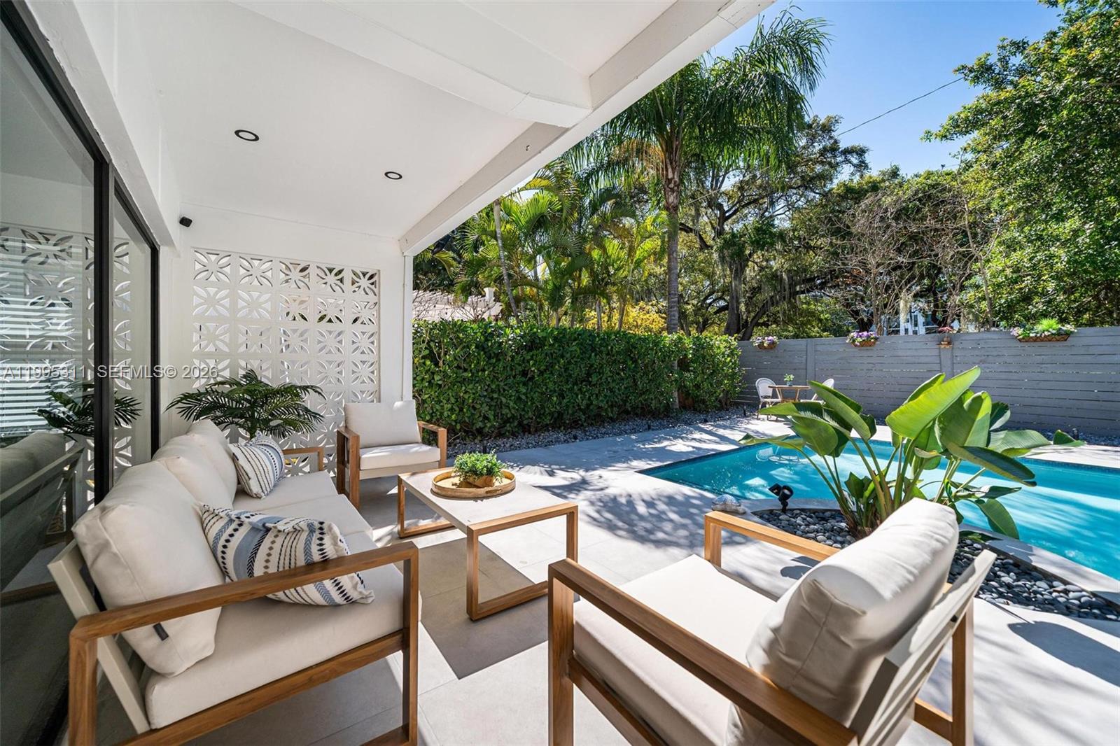A covered patio features outdoor furniture, a decorative screen, and a swimming pool in the yard — 696 NE 67th St, Miami FL 33138, MIAMI, FL