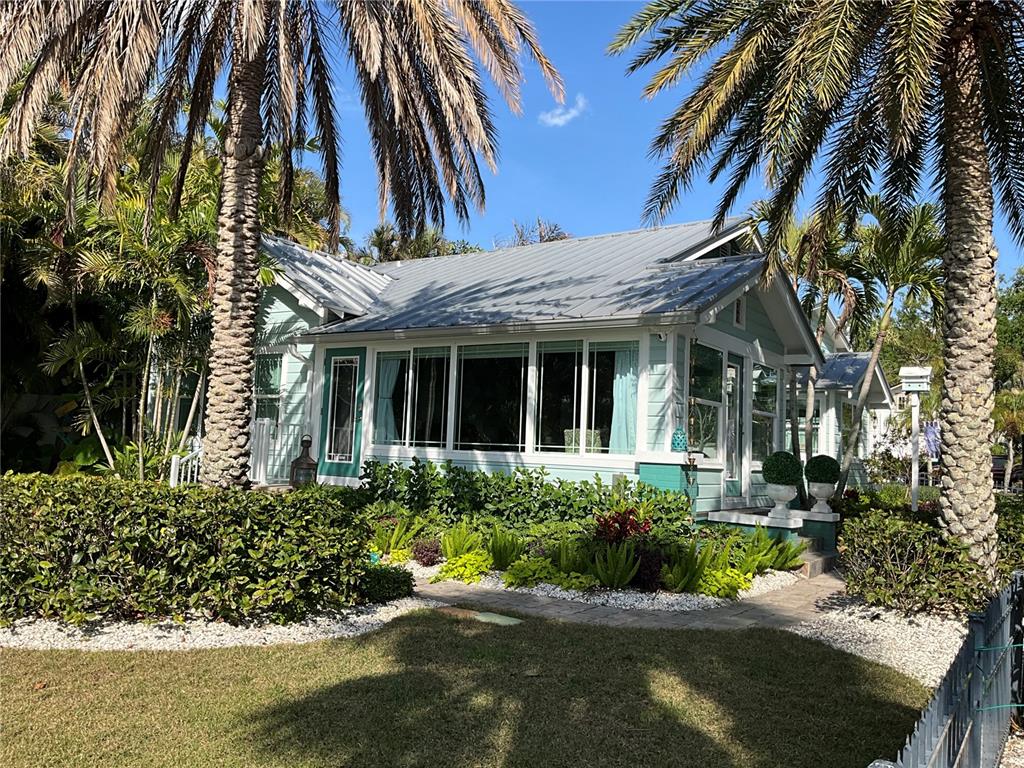 A light blue cottage with a metal roof surrounded by palm trees and lush landscaping — 202 FAIRMONT STREET, CLEARWATER, FL
