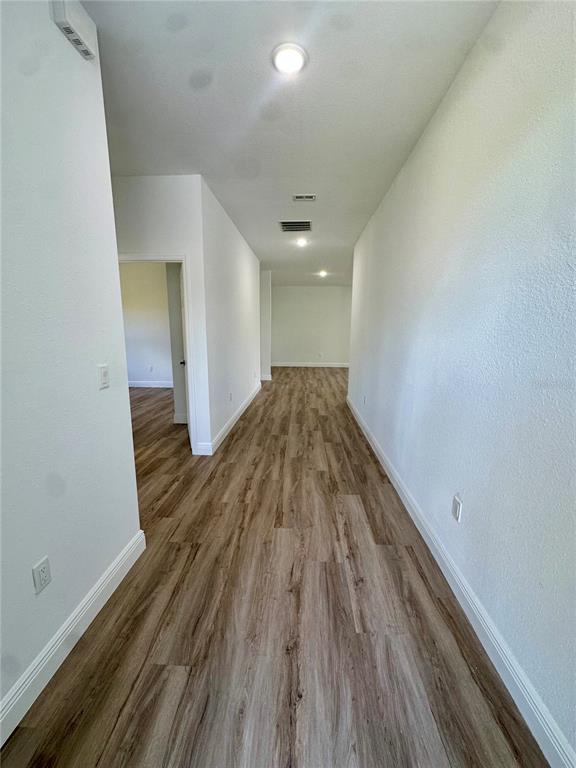 A long, empty hallway features light-colored walls, wood-look flooring, and recessed ceiling lighting — 8533 LANCELOT AVENUE, NORTH PORT, FL