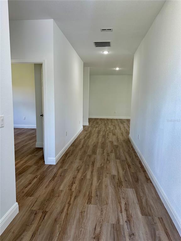 A hallway with light wood-look flooring leads to an open room with white walls — 8533 LANCELOT AVENUE, NORTH PORT, FL