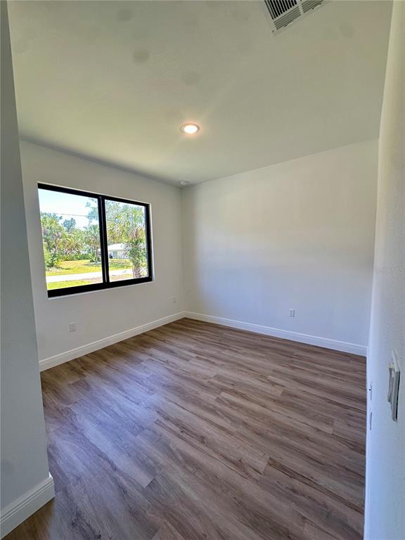 An empty room features light wood-look flooring, white walls, and a window overlooking greenery — 8533 LANCELOT AVENUE, NORTH PORT, FL