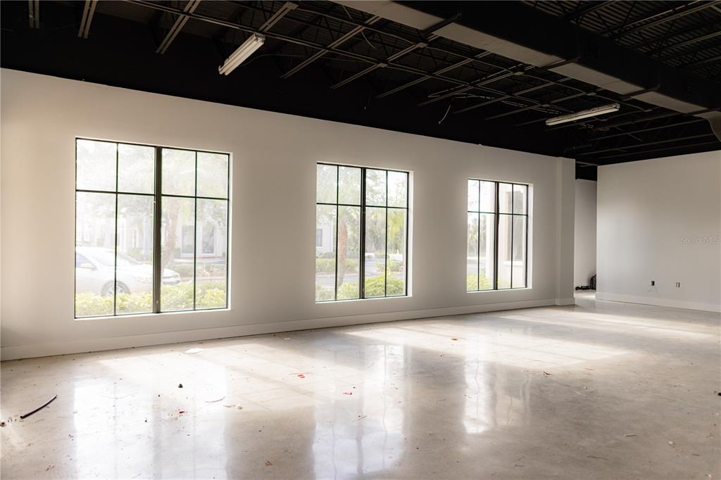 An empty commercial space features white walls, a black industrial ceiling, and large grid windows — 5920 PAN AMERICAN BOULEVARD UNIT 101, NORTH PORT, FL