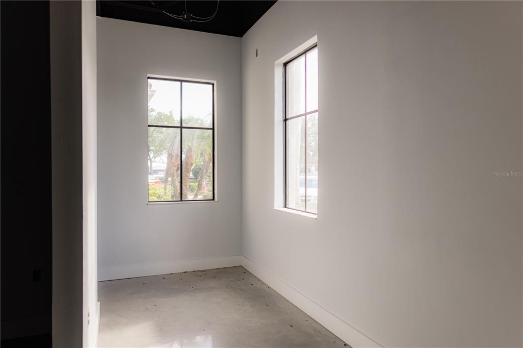 An empty room with light gray walls, concrete floors, and two large grid-style windows — 5920 PAN AMERICAN BOULEVARD UNIT 101, NORTH PORT, FL
