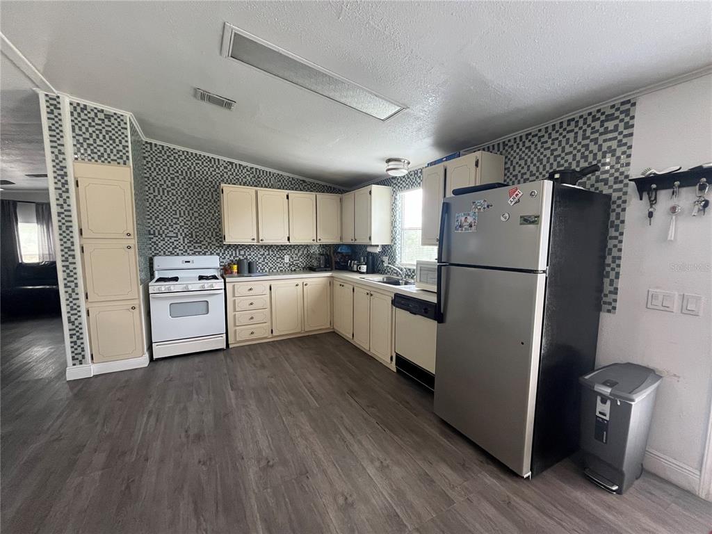 A kitchen features light-colored cabinets, a stainless steel refrigerator, a white stove, and patterned backsplash — 10780 STATE ROAD 60 E, LAKE WALES, FL
