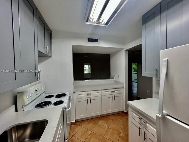 A kitchen features gray upper cabinets, white lower cabinets, a white stove, and tiled floors — 10755 SW 108th Ave # 302, Miami FL 33176, MIAMI, FL