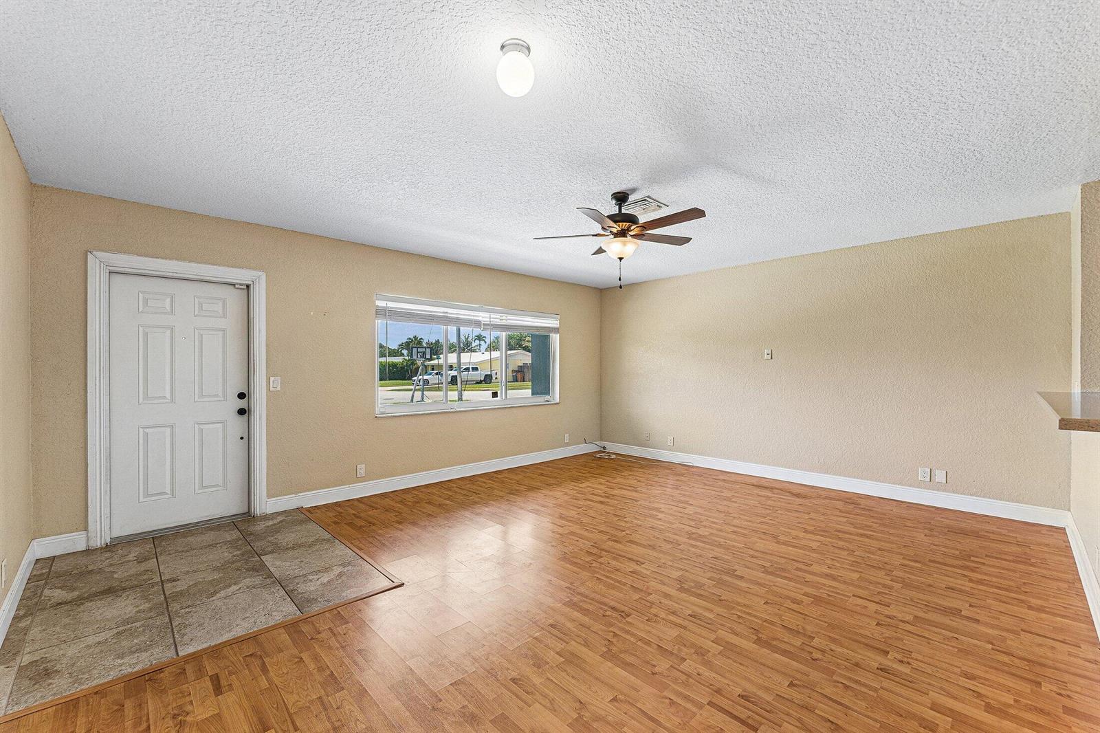 An empty living room features wood-look flooring, a ceiling fan, and a front entry door — 301 SE 3rd Street, Deerfield Beach FL 33441, DEERFIELD BEACH, FL