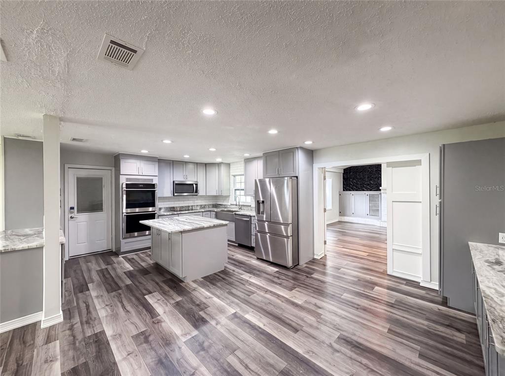 A modern kitchen features gray cabinets, stainless steel appliances, a marble-topped island, and wood-look flooring — 1823 LORI LANE W, LAKELAND, FL