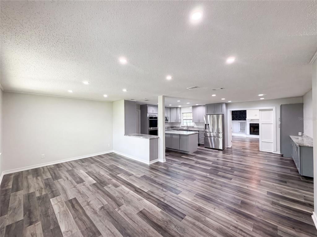 An open-concept kitchen and living area with gray cabinetry, stainless appliances, and wood-look flooring — 1823 LORI LANE W, LAKELAND, FL