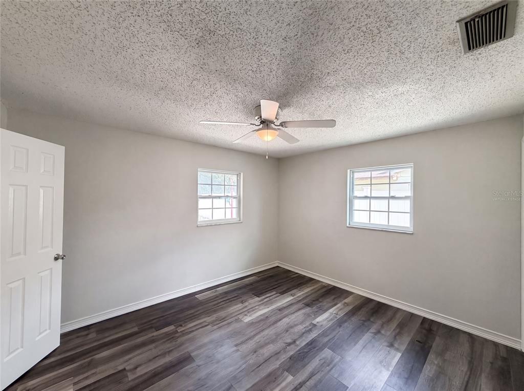 An empty bedroom features light gray walls, dark wood-look flooring, and a ceiling fan — 1823 LORI LANE W, LAKELAND, FL