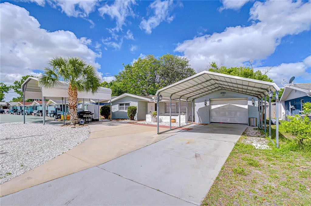 A single-story house features a concrete driveway, a metal carport, and a palm tree — 10901 OLDHAM ROAD, PORT RICHEY, FL