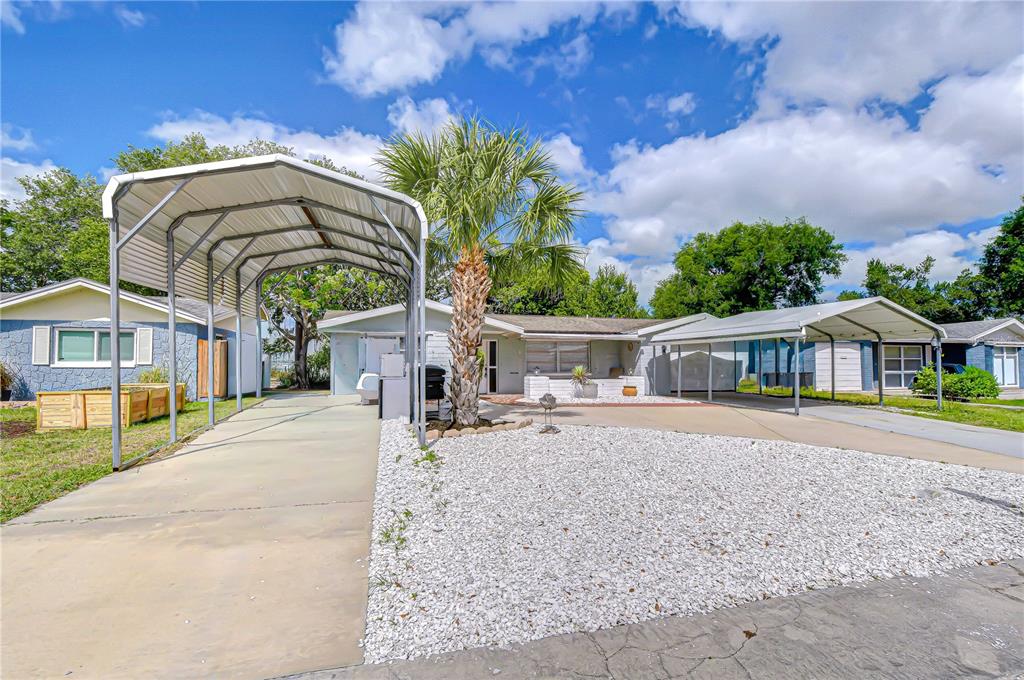 A single-story house features two metal carports, a palm tree, and a white gravel yard — 10901 OLDHAM ROAD, PORT RICHEY, FL