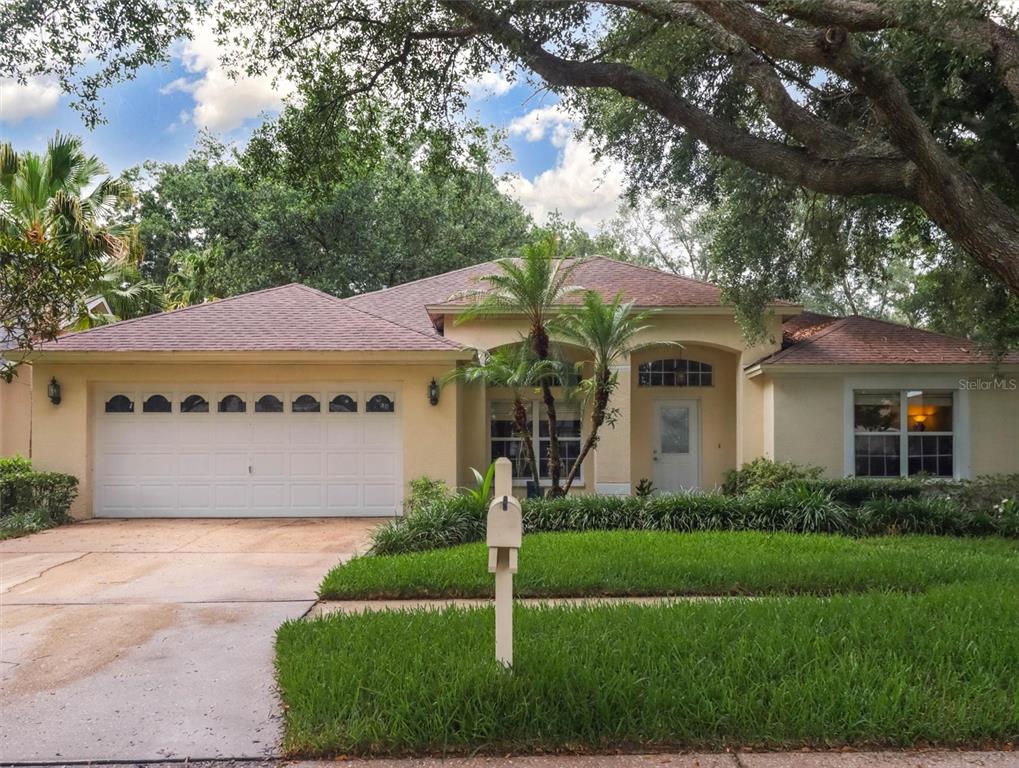 A single-story house with a two-car garage, a front lawn, and mature trees — 10110 WHISPER POINTE DRIVE, TAMPA, FL