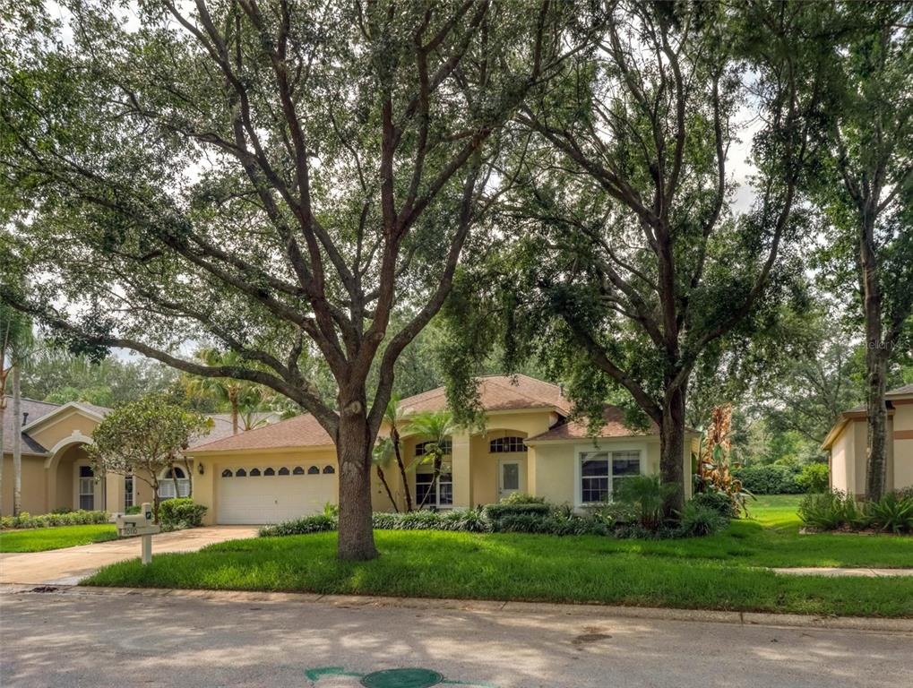A single-story house with a two-car garage sits behind two large trees on a lawn — 10110 WHISPER POINTE DRIVE, TAMPA, FL