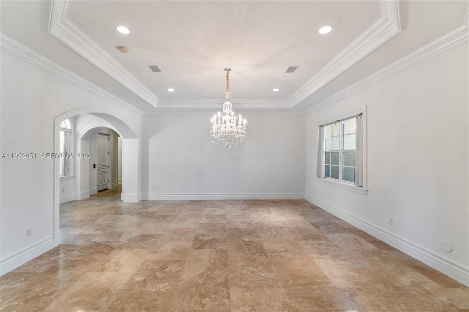 An empty dining room features a crystal chandelier, tray ceiling, and light brown tile flooring — 6025 SW 108th St, Pinecrest FL 33156, PINECREST, FL