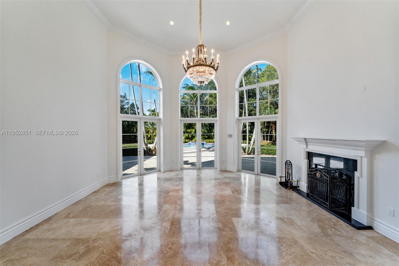 A bright living room features a crystal chandelier, arched windows, and polished stone flooring — 6025 SW 108th St, Pinecrest FL 33156, PINECREST, FL