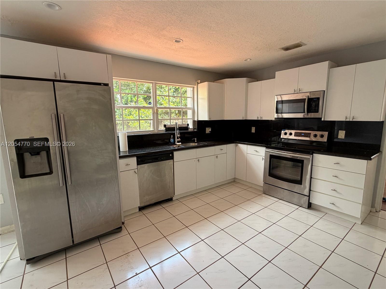 A kitchen features white cabinets, black countertops, stainless steel appliances, and white tiled flooring — 14444 SW 92nd Ter # 14444, Miami FL 33186, MIAMI, FL