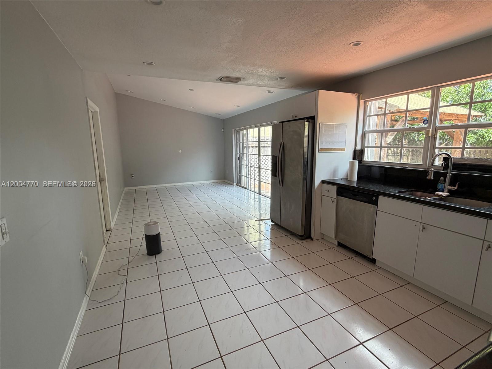 A kitchen with white cabinets and black countertops opens into a tiled living area — 14444 SW 92nd Ter # 14444, Miami FL 33186, MIAMI, FL