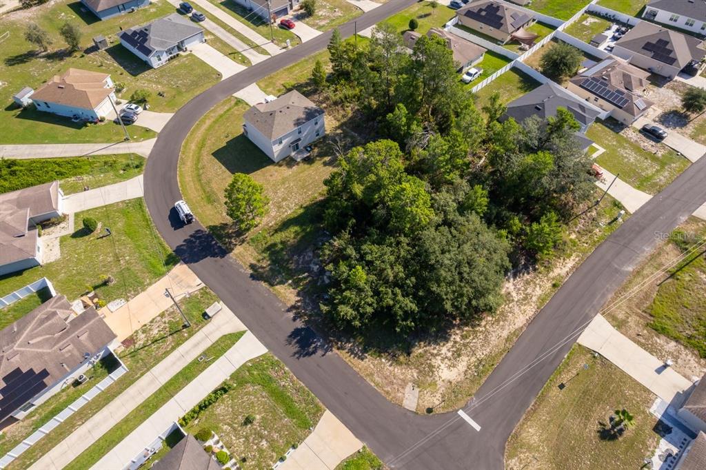 An aerial view shows a wooded vacant lot situated between several suburban residential homes — 174 MAPLE DRIVE, POINCIANA, FL