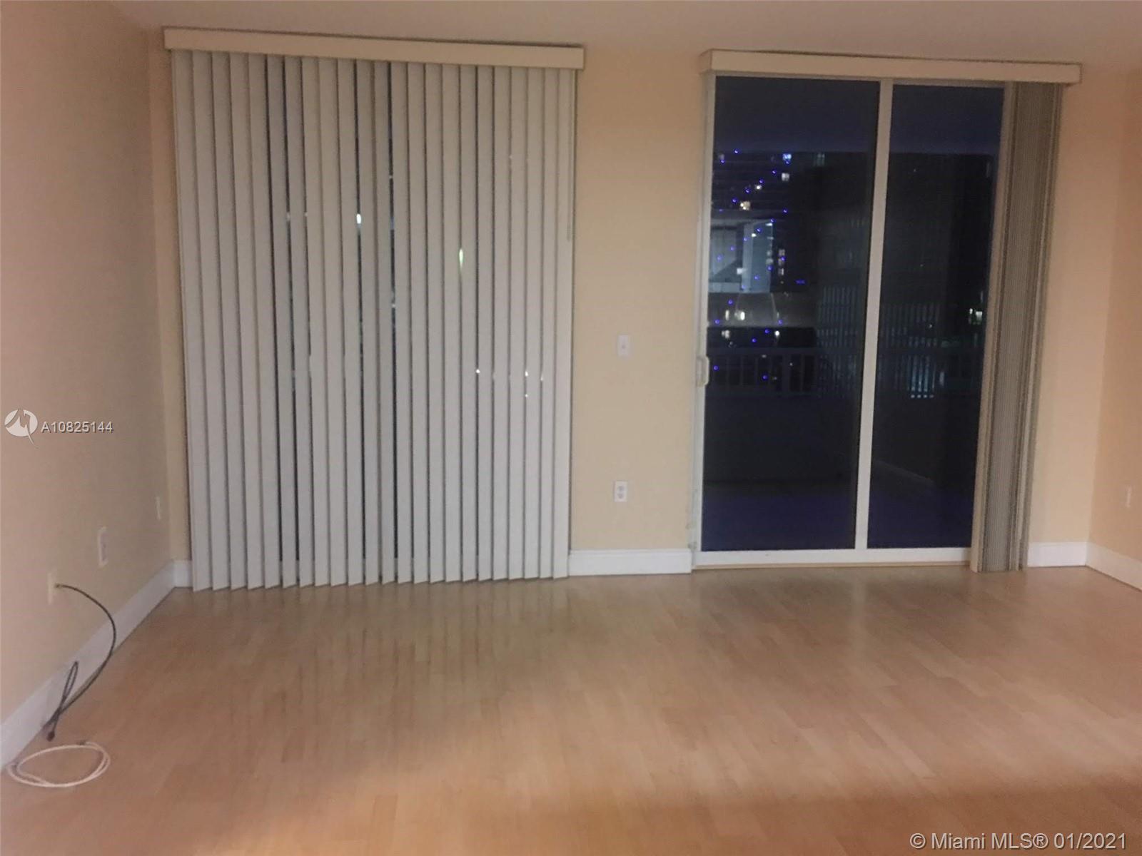 An empty room features light wood flooring, beige walls, vertical blinds, and a sliding glass door — 170 SE 14th St # 1507, Miami FL 33131, MIAMI, FL