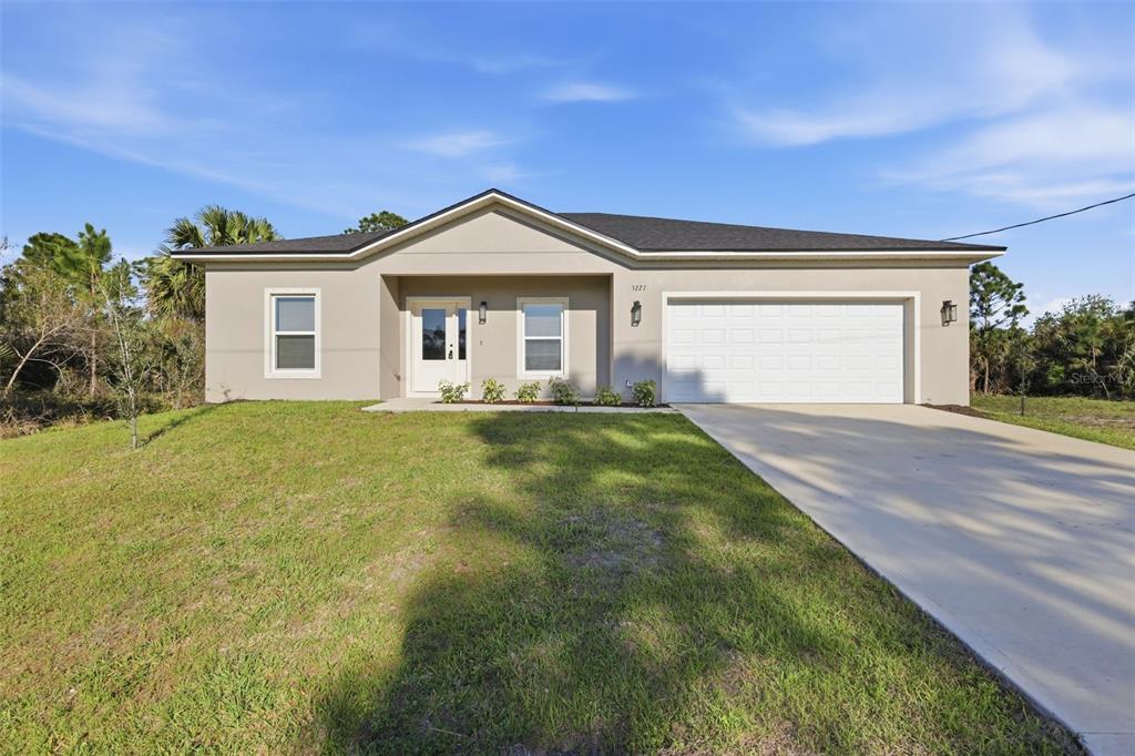 A single-story house with a beige stucco exterior, a white garage door, and a concrete driveway — 3227 HALSEY AVENUE SE, PALM BAY, FL