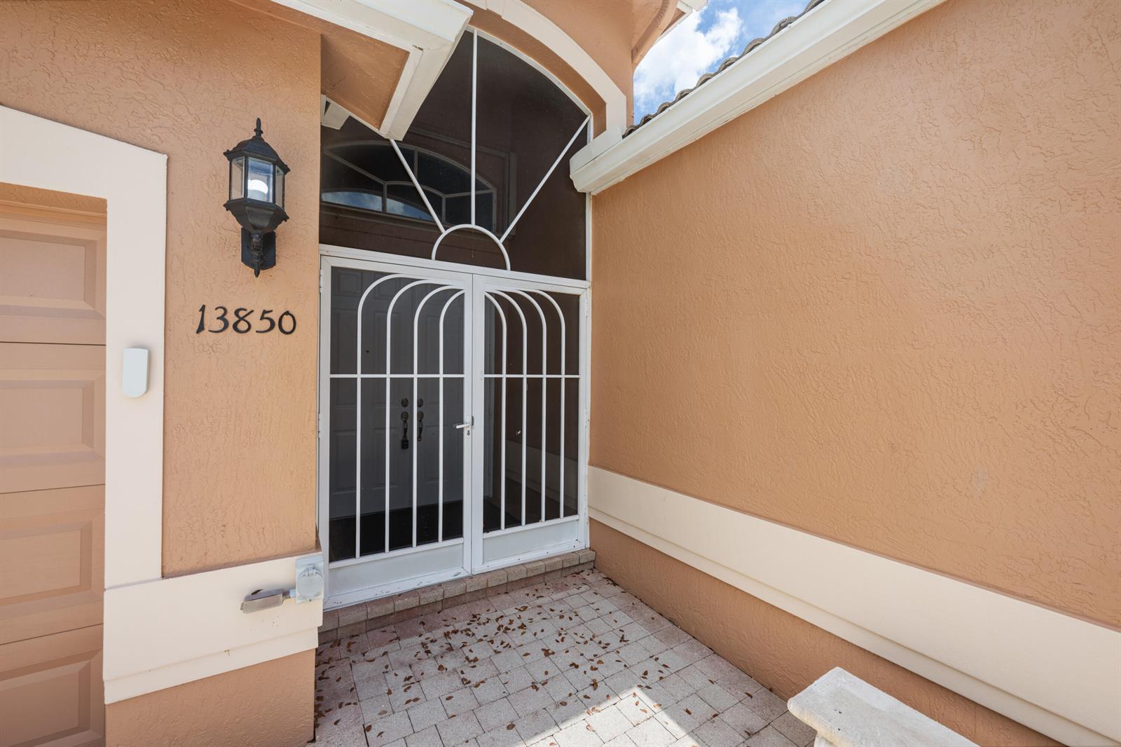 A front entryway features a white metal security screen door and a matching arched transom — 13850 Vía Vittoria, Delray Beach FL 33446, DELRAY BEACH, FL