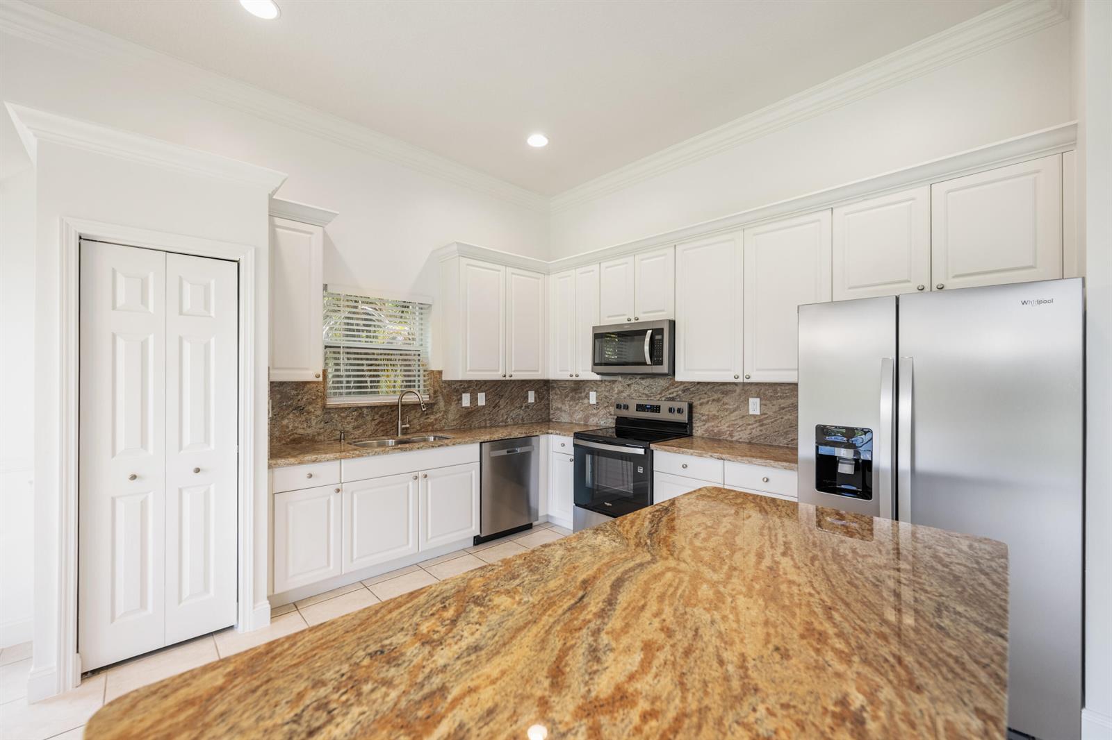A kitchen features white cabinets, granite countertops, stainless steel appliances, and a large center island — 13850 Vía Vittoria, Delray Beach FL 33446, DELRAY BEACH, FL