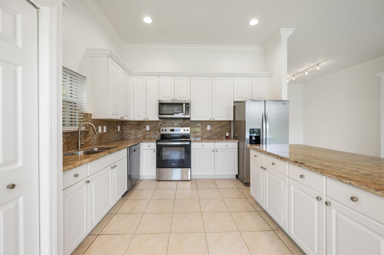 A kitchen features white cabinets, granite countertops, stainless steel appliances, and beige tile flooring — 13850 Vía Vittoria, Delray Beach FL 33446, DELRAY BEACH, FL
