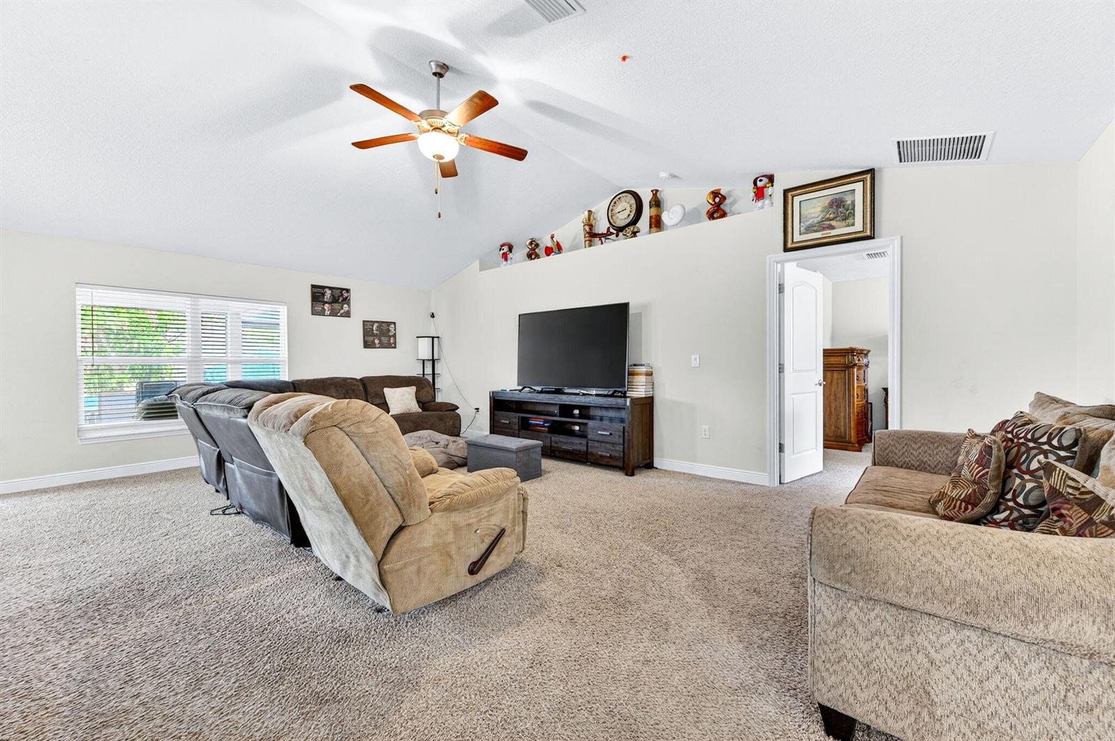 A living room features vaulted ceilings, a ceiling fan, carpeted floors, and a television console — 1726 Pace Drive NW, Palm Bay FL 32907, PALM BAY, FL