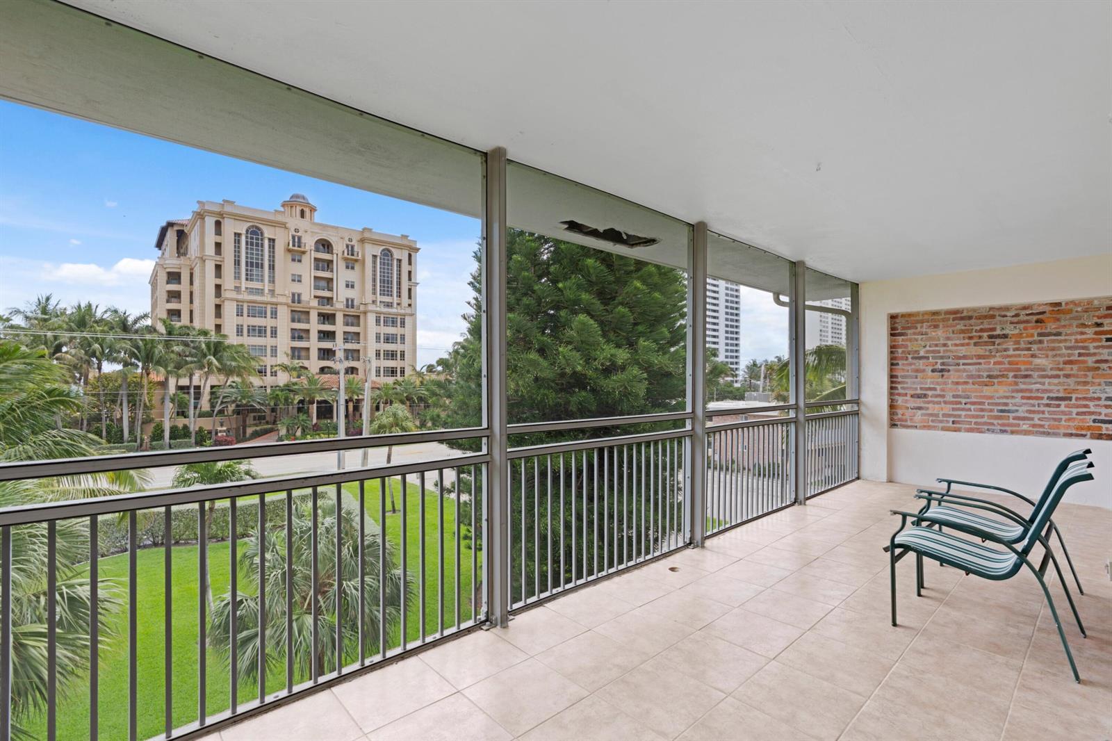 A screened-in balcony features tiled flooring, a brick accent wall, and views of nearby buildings — 2501 S Ocean Boulevard # 3010, Boca Raton FL 33432, BOCA RATON, FL