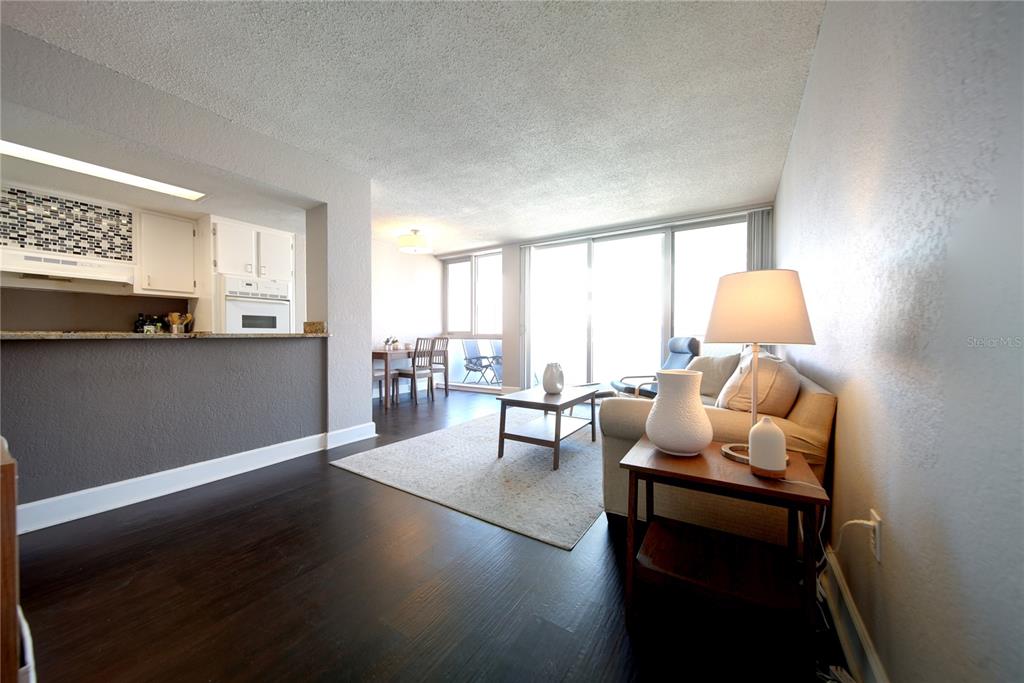 A living room with dark wood floors, a beige sofa, and an adjacent kitchen area — 470 3RD STREET S UNIT 612, ST PETERSBURG, FL