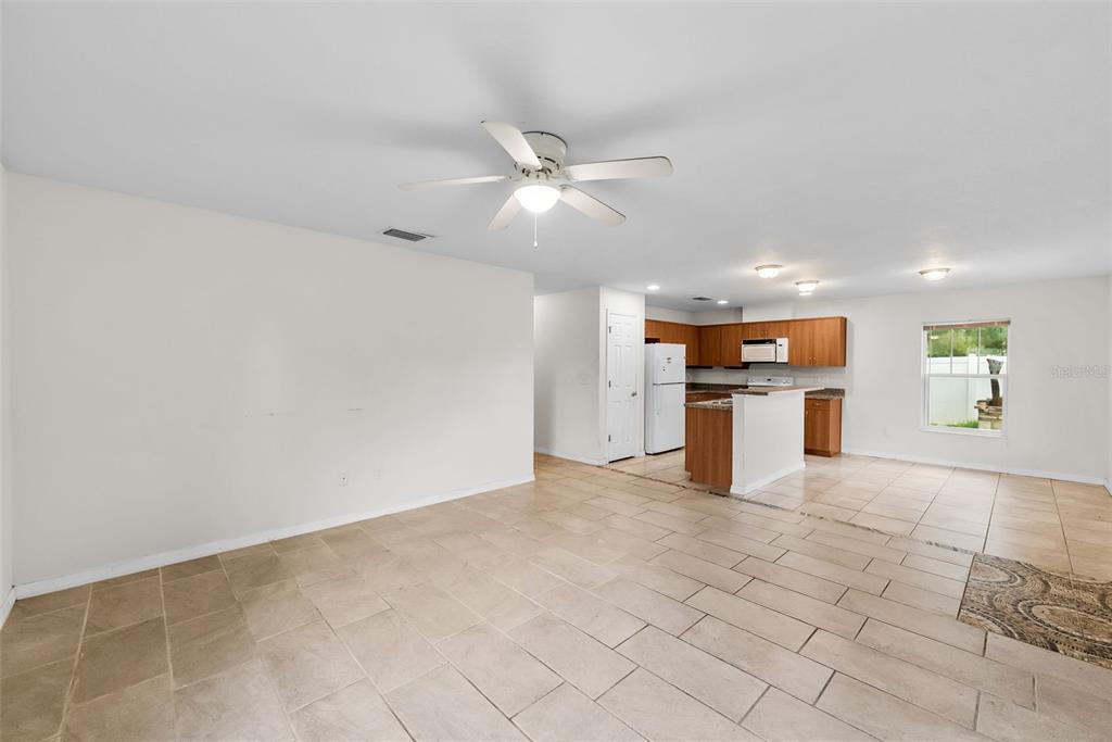 An open-concept living area features light-colored tile flooring, a ceiling fan, and a kitchen — 5451 MAC ARTHUR AVENUE, NEW PORT RICHEY, FL